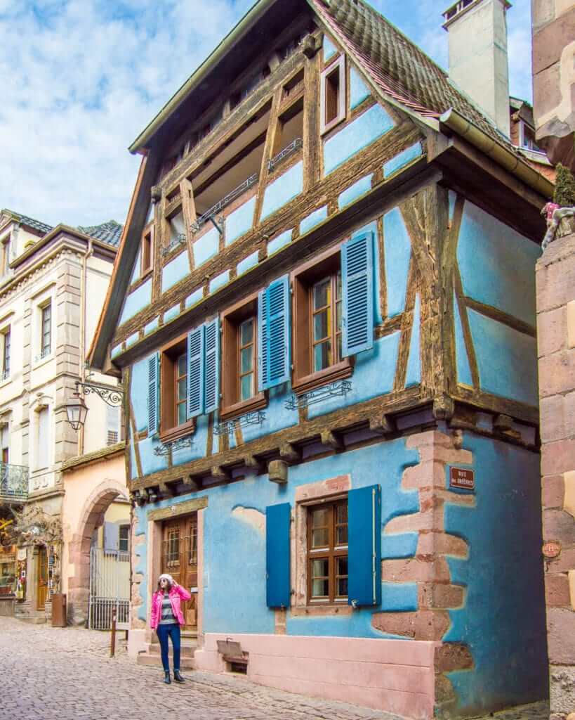 Woman walking in front of historic home in Riquewihr, France