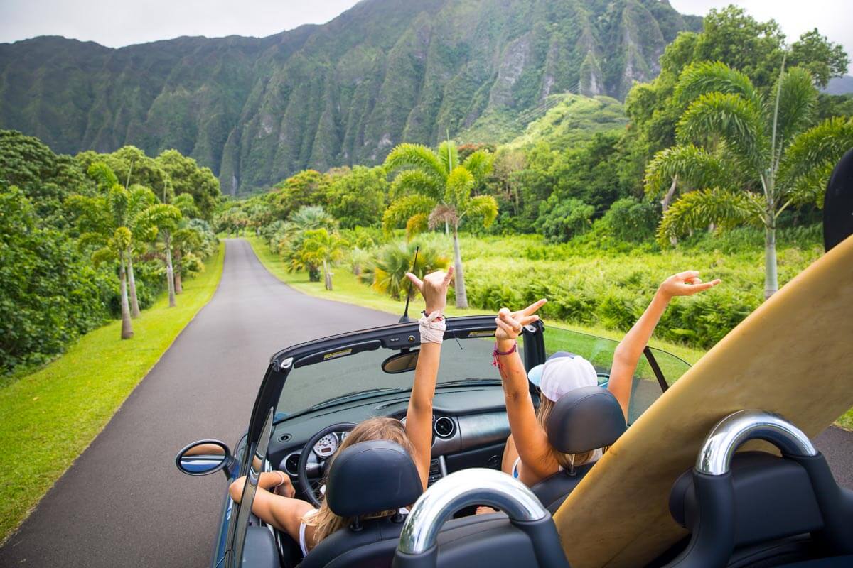 Women with their arms in the air in a convertible posing in Ho'omaluhia Botanical Garden in Oahu, Hawaii