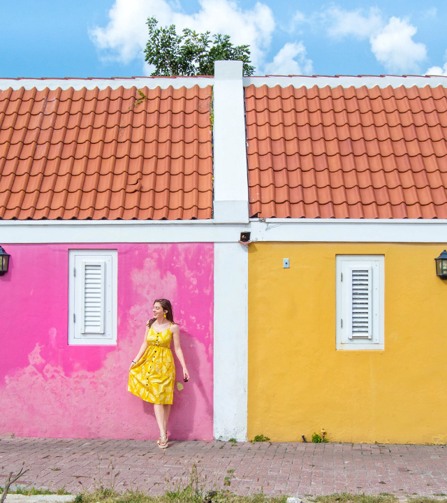 Woman in front of pink and yellow houses in Willemstad, Cura&ccedil;ao