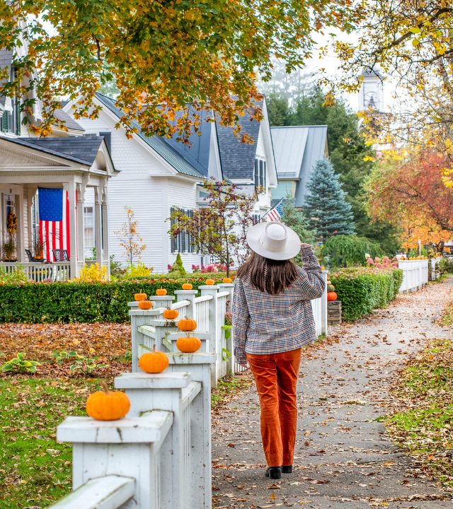 Woman walking down historic street in Woodstock Village, Vermont, which is decorated for Halloween with pumpkins