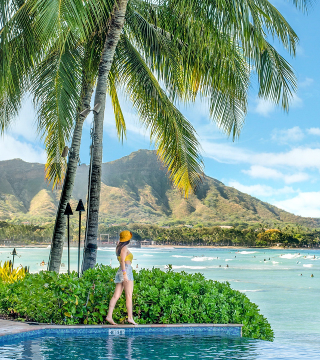 Woman next to infinity pool at the Sheraton Waikiki hotel with Diamond Head and Waikiki Beach in the distance.