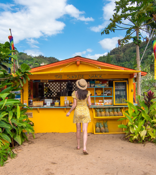 Woman in yellow dress with back to camera walking to The Sunrise Shack, a yellow shop across from Sunset Beach, North Shore, Oahu, Hawaii.