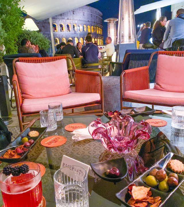 The Court cocktail bar, with snacks and drinks and a view of the Colosseum in the background.