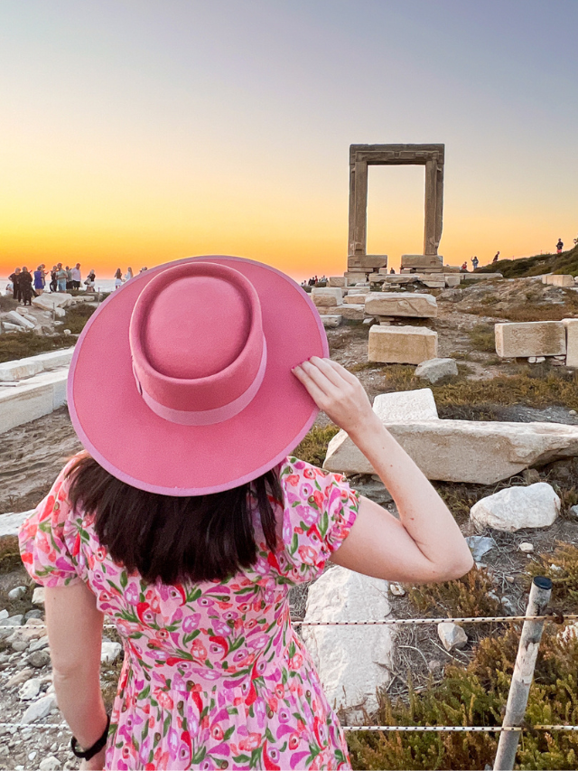 Woman wearing pink hat watching the sunset at the Portara on the Greek island of Naxos