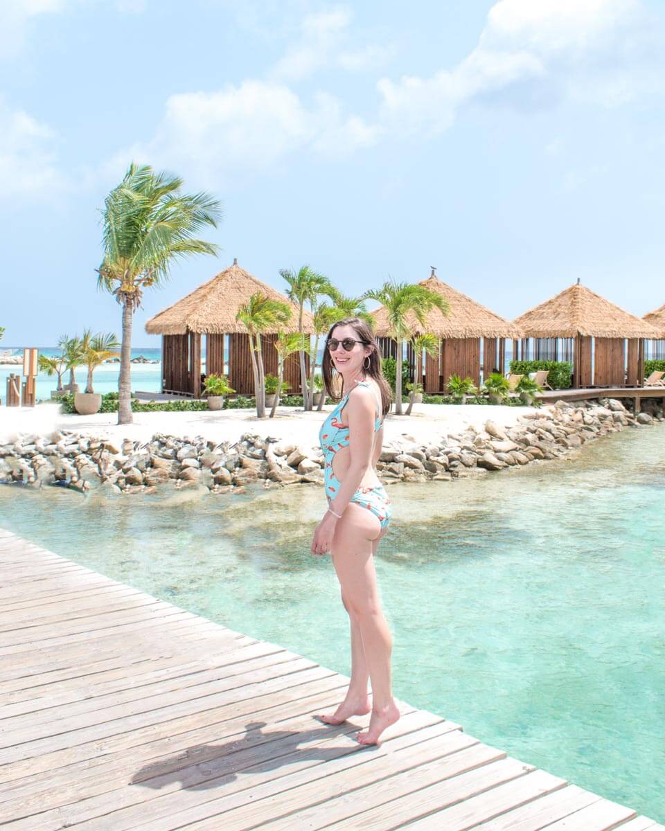 Woman standing on pier over water in front of private cabanas on Renaissance Island in Aruba.